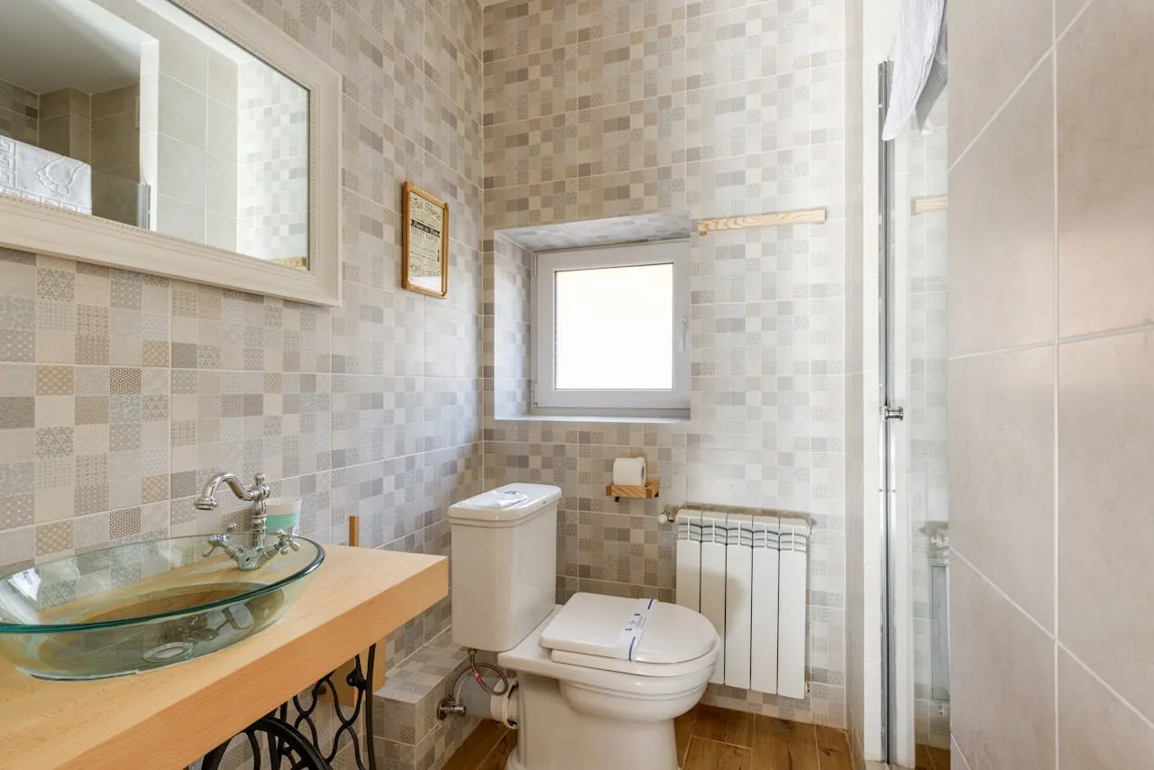 Aseo con azulejo tipo mosaico beige y lavabo de vidrio