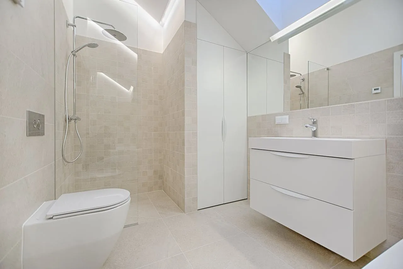 Salle de bain beige sous combles avec douche ouverte et meuble blanc