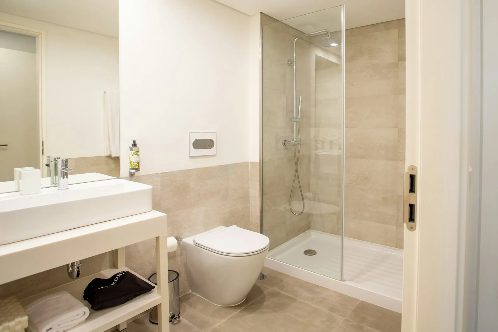 Baño beige con ducha acristalada, inodoro suspendido y lavabo