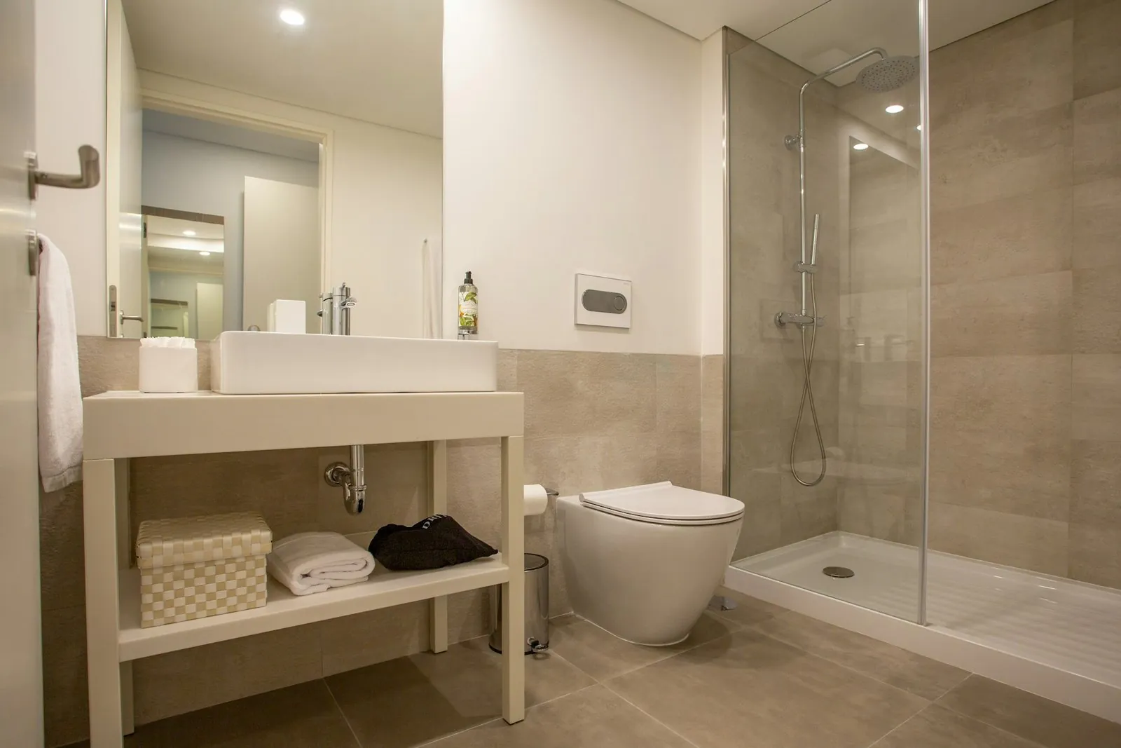 Baño beige con plato de ducha, mampara fija y mueble lavabo abierto