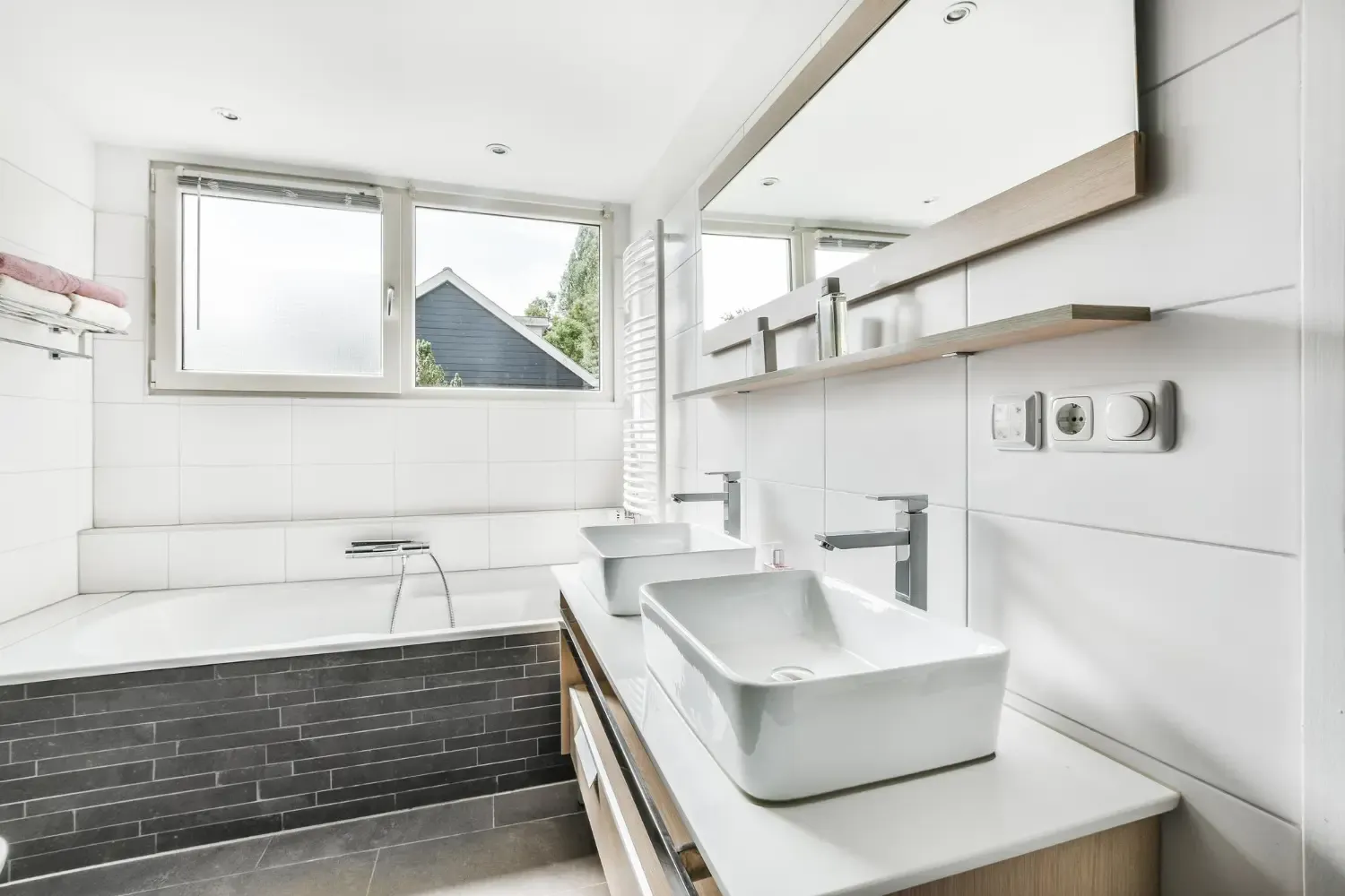 Baño blanco con bañera revestida de piedra y doble lavabo
