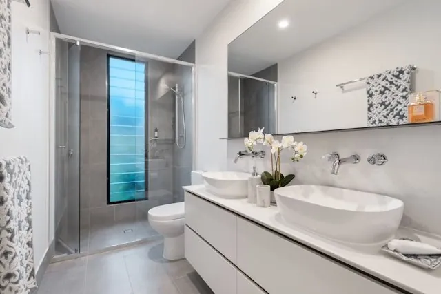 Baño blanco con doble lavabo sobre encimera y ducha acristalada