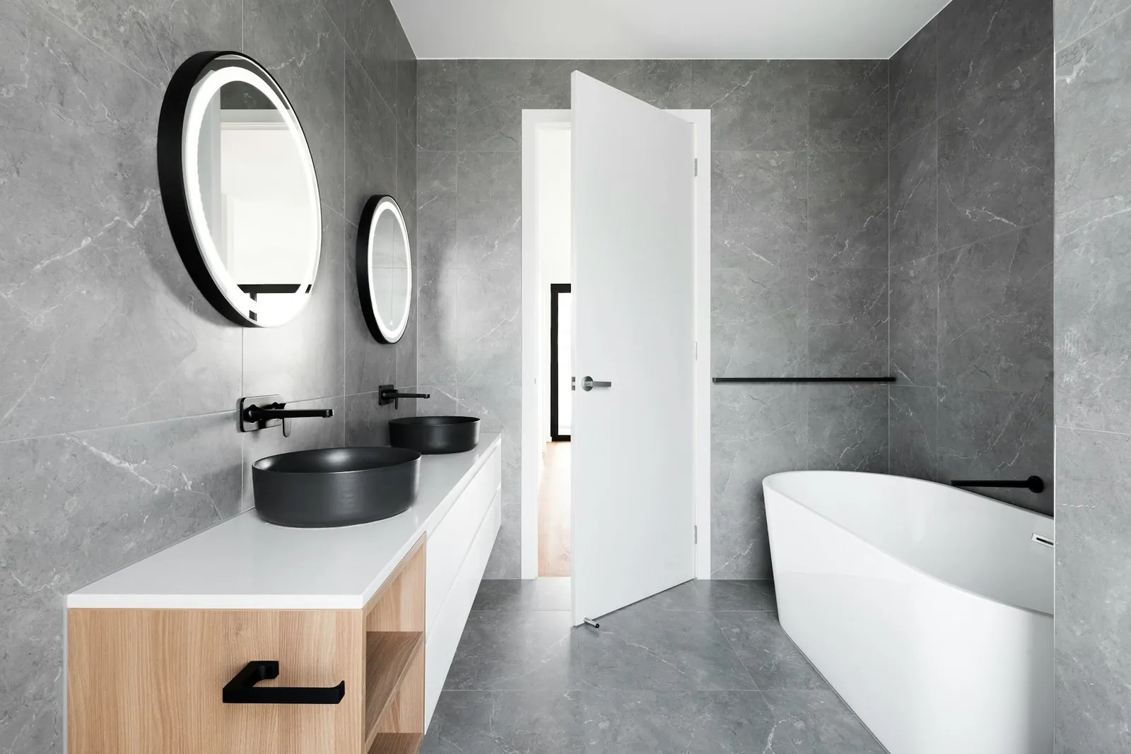 Baño gris con bañera exenta, lavabos negros y espejos LED redondos