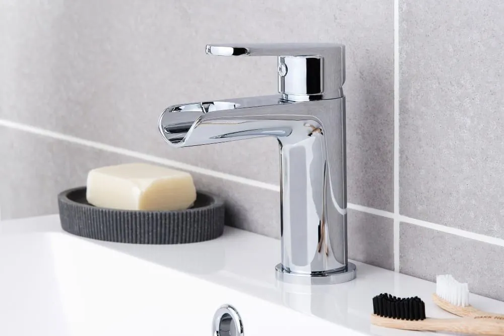 Grifo cascada cromado sobre lavabo con jabonera