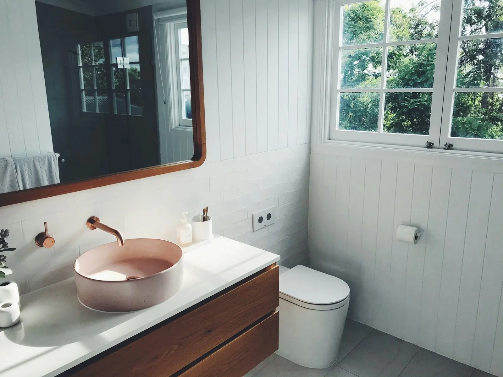 Lavabo rosa sobre mueble de madera con grifería cobre y ventana
